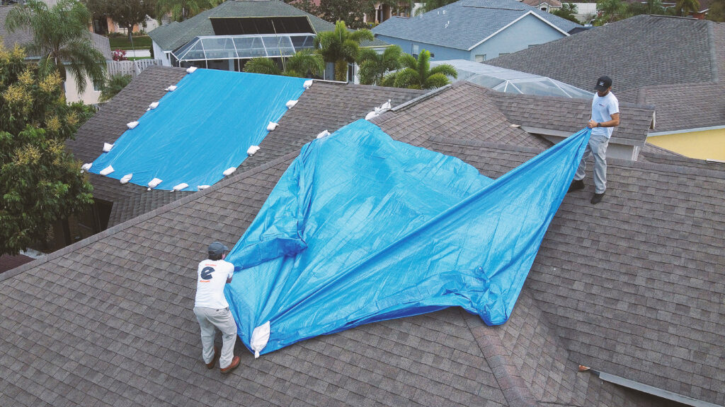 Workers putting a tarp on a roof to prevent water damage from rain